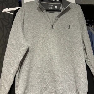 Grå half zip tröja Polo Ralph Lauren - Snygg grå långärmad tröja från Polo Ralph Lauren med klassisk half zip-dragkedja och broderad logga på bröstet. Enkel och stilren design som funkar året runt!