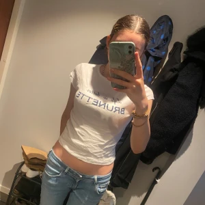 Vit croppad t-shirt med tryck - Säljer en vit croppad t-shirt med blå texten 'Life is better BRUNETTE' på bröstet. T-shirten har korta ärmar och en tight passform. Perfekt för dig som gillar statement-plagg och vill ha en enkel men snygg look.