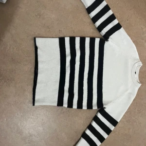 Randig stickad tröja från H&M Divided XS - Säljer en snygg stickad tröja från H&M Divided i storlek XS. Tröjan är oversized. Tröjan är vit med breda svarta ränder på både ärmar och kropp. Den har rund halsringning och ribbade muddar. Perfekt för dig som gillar en klassisk men trendig look.