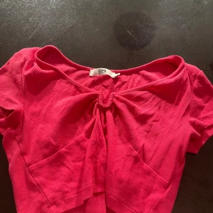 Ribbad rosa topp från CPS Chaps - Säljer en ribbad rosa topp från CPS Chaps i storlek XS. Toppen har korta ärmar, en snygg knytdetalj framtill och en croppad passform. Perfekt för dig som gillar färgstarka och trendiga plagg.