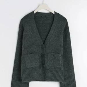 Mörkgrå kofta från Gina Tricot - Mysig mörkgrå kofta från Gina Tricot med v-ringning, stora knappar och två rejäla fickor framtill. Koftan är stickad och har långa ärmar samt breda ribbade muddar vid ärmslut och nederkant. Perfekt för lager-på-lager under kyliga dagar.