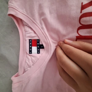 Rosa t-shirt från Tommy Jeans - Snygg ljusrosa t-shirt från Tommy Jeans med röd logga framtill. Klassisk rund halsringning och korta ärmar. Tillverkad i mjuk bomull som känns skön mot huden. Perfekt för en chill och avslappnad stil.