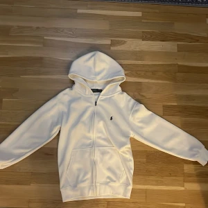Vit zip hoodie från Polo Ralph Lauren - Snygg vit hoodie från Polo Ralph Lauren med dragkedja och klassisk broderad logga på bröstet. I ny skick har används ett par gånger bara, säljer pga av att jag inte gillar den längre. Pris kan diskuteras vid snabb affär.
