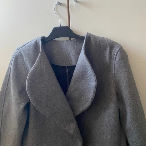 Grå omlottkappa från hm XXS passar mig som brukar ha S  - Snygg grå kappa från H&M i omlottmodell med rundad krage och stilren design. Jackan har långa ärmar. Perfekt för dig som gillar minimalistisk och clean stil.