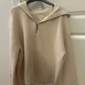 Beige stickad hoodie med half zip - Supermysig beige stickad hoodie med ribbad struktur och halv dragkedja framtill. Tröjan har en avslappnad passform, huva och långa ärmar.