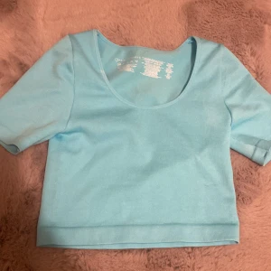 Ljusblå croppad topp från Primark -  ljusblå croppad topp från Primark med rundad, djup urringning och korta ärmar. Toppen är ribbad och har en tight passform, tillverkad i mjukt och stretchigt material och är i storlek xs, aldrig använt 