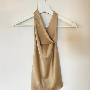 Beige halterneck i satin biege guld XS Zara - Snygg beige halterneck i satinliknande material med draperad framsida och öppen rygg. Populär och helt slutsåld! Aldrig använd. Storlek Xs, normal i storleken.🤩 