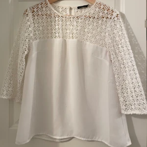 Vit spetsblus från Stockh LM - Superfin vit blus från Stockh LM med blommig spets upptill och på ärmarna. Blusen har trekvartsärm och rund halsringning. Nederdelen är slät och mjuk, medan överdelen och ärmarna är helt i spets med blommönster. Perfekt för dig som gillar romantisk stil.