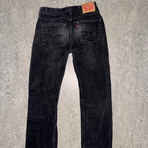 Levi's 501 svarta jeans straight fit - Svarta Levi's 501 jeans med klassisk straight fit och femficksdesign. Jeansen har en vintage tvätt och ikonisk läderpatch bak i midjan. Tillverkade i slitstarkt jeanstyg med normal passform och raka ben. Perfekta för en avslappnad och tidlös stil. kan gå ner i snabbt köp 