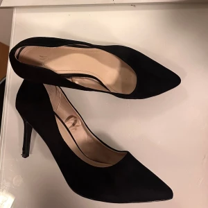 Svarta pumps med spetsig tå - Snygga svarta pumps med spetsig tå och klack. Skorna har en elegant och klassisk design i mockaliknande material och passar perfekt när du vill lyfta din outfit. Bekväm innersula och stilren look som funkar till många olika stilar.