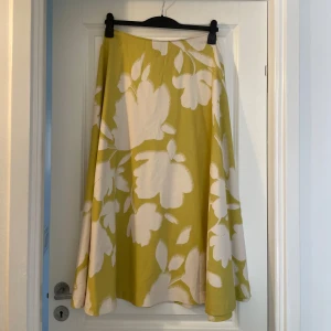 Blommig långkjol från Lindex - Säljer en flowy långkjol från Lindex i storlek 38. Kjolen har ett stort blommigt mönster i vitt och gult, perfekt för dig som gillar färg och vill sticka ut. Den har en vid och svepande passform som ger en riktigt skön känsla.