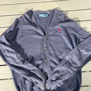 Mörkblå kofta från Polo Ralph Lauren - Snygg mörkblå kofta från Polo Ralph Lauren med klassisk röd logga broderad på bröstet. Koftan har v-ringning, långa ärmar och knäppning med fem knappar framtill. Perfekt för lager-på-lager och chill stil.