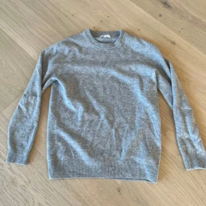 Grå stickad tröja i kashmir - Mjuk och stilren grå stickad tröja i kashmir med rund halsringning och ribbade muddar vid ärmslut och nederkant. Perfekt för lager-på-lager och enkel att matcha med jeans.