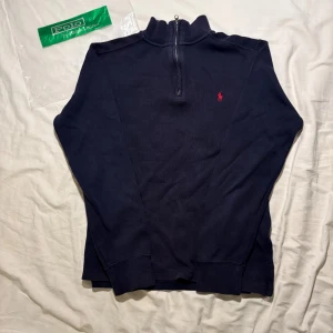 Marinblå half zip tröja Polo Ralph Lauren - Säljer en marinblå långärmad tröja från Polo Ralph Lauren med röd broderad logga på bröstet. Tröjan har half zip-dragkedja vid halsen och är gjord i mjuk bomull. Perfekt för lager-på-lager och snygg till jeans. För barn 