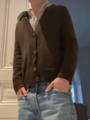 Brun stickad kofta med knappar - Mysig brun stickad kofta i storlek Xs med stora bruna knappar och två fickor framtill. Koftan har ribbade muddar vid ärmslut och nederkant samt en liten krage. Perfekt för lager på lager och chill stil. passar om man är 165-175~ däremot så har den flera hål på ryggen.