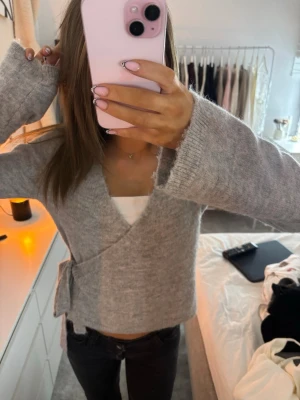 Grå omlottkofta med knyt - Mysig grå omlottkofta i mjukt stickat material. Koftan har långa ärmar och knyts i sidan för en snygg och avslappnad look. 