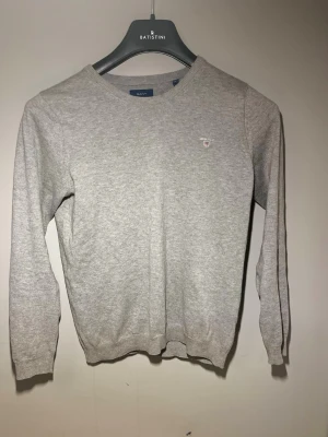 Grå stickad tröja från GANT - Snygg grå stickad tröja från GANT säljes. Tröjan är köpt för 600 kr men säljs för 199 kr. Den är i mycket bra skick då den har använts försiktigt, utan några skador – endast lätt nött, så gott som nyskick. Storlek dam XS (motsvarar ca 158) och passar lika bra på killar. Hör gärna av dig vid intresse!