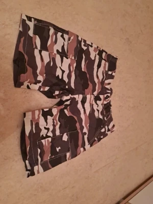Camo shorts från Warp, storlek S - Jag säljer ett par shorts i storlek S som är i helt nytt skick. De är aldrig använda och perfekta för dig som vill ha ett par nya shorts till ett bra pris.  Priset är 100 kr, vilket jag tycker är ett riktigt bra pris med tanke på att de är helt nya. Jag är öppen för snabba affärer!  Tveka inte att höra av dig om du är intresserad eller har några frågor. Först till kvarn gäller!