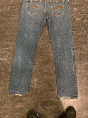 Blå raka jeans nudie jeans - Snygga blå jeans med raka ben och rå, fransig kant nertill. Klassisk femficksmodell med kontrastsömmar och coola detaljer på bakfickorna. Perfekta för en avslappnad och trendig look.