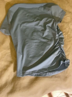 Ljusblå topp med snörning i sidan - Säljer en ljusblå topp med korta ärmar och snygg snörningsdetalj i sidan. Toppen har en enkel, clean look och är gjord i mjukt bomullsmaterial. Perfekt för dig som gillar stilrena plagg med en twist.