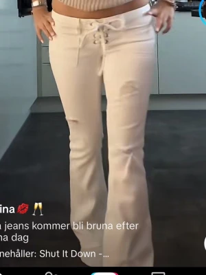 Vita bootcut jeans med snörning - Säljer ett par vita bootcut jeans med snygg snörning framtill i midjan. Jeansen har en hög midja och är tillverkade i ett stretchigt jeansmaterial som sitter bekvämt. Perfekta för dig som vill ha en unik twist på klassiska jeans.