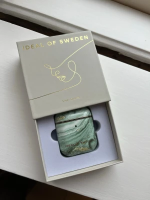 Grön AirPods-fodral Ideal of Sweden - Snyggt AirPods-fodral från Ideal of Sweden i mönstret Clear Quartz. Fodralet har en grön marmorerad look med gulddetaljer och passar AirPods Gen 1 & 2. Tillverkat i hårdplast och levereras i originalförpackning.