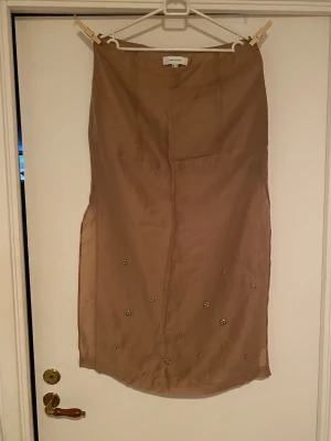 Beige långkjol med pärldetaljer - Snygg beige långkjol från Gina Tricot i ett tunt, lätt material. Kjolen har dekorativa pärldetaljer i blommönster nedtill som ger en unik touch. Perfekt för dig som vill ha något stilrent men ändå speciellt.