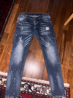 Mörkblå jeans från Dsquared2 - Säljer ett par mörkblå skinny jeans från Dsquared2 med coola färgstänk och slitningar. Inga slitningar eller skador. 