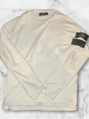 Beige  tröja från Stone Island - Säljer en beige  tröja från Stone Island med klassisk rund hals och lång ärm. Tröjan har den ikoniska avtagbara Stone Island-patchen på ärmen, både i svart och gult. Perfekt för dig som gillar stilrena och exklusiva plagg. Skick 10/10 såklart äkta ‼️‼️