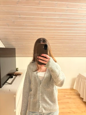 Ljusgrå kofta från Bik Bok - Mysig ljusgrå kofta från Bik Bok med v-ringning och fyra knappar framtill. Koftan har långa ärmar och ribbade muddar vid ärmslut och nederkant. Perfekt att slänga över en topp för en chill look.