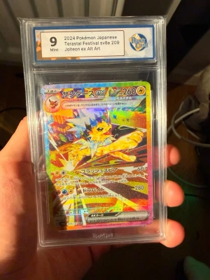 Jolteon ex Alt Art Pokémonkort 2024 - Japanskt Pokémonkort från 2024, Jolteon ex Alt Art Terastal Festival sv8a 209. Kortet är graderat Mint 9 av RaukCard och har en färgstark, holografisk design med Jolteon i action. Kortet ligger i ett genomskinligt plastskydd.