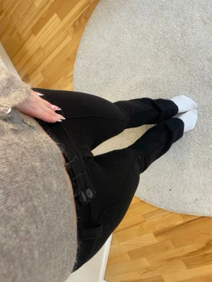 Svarta bootcut kostymbyxor med knappar - Säljer ett par svarta bootcut byxor med två knappar i midjan. Byxorna har en fin och tight passform och är tillverkade i ett stretchigt material. De är i storlek 158 men passar perfekt för mig som brukar ha xs/s i byxor är 163 för referens!!!💕💕de är även helt oanvända!