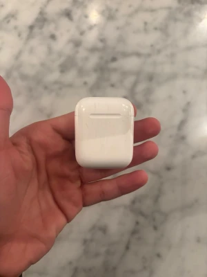 Apple AirPods med laddningsetui - Säljer ett par vita Apple AirPods med det klassiska laddningsetuiet. Smidig och kompakt design i blank plast som är enkel att ta med sig överallt. Perfekt för musik, poddar och samtal utan sladdar.