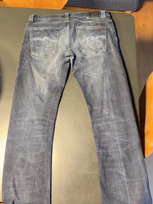 Blå nudie jeans slim fit/lean dean - Säljer ett par klassiska blå jeans från nudie Jeansen har slitningar och ljusare partier för en cool look. Obs den har ett hål inne i ena fickan men de går att fixas