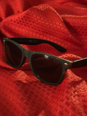 Svarta klassiska solglasögon - Snygga svarta solglasögon med klassisk wayfarer-form. Bågarna är helsvarta med små silvriga detaljer vid fronten. Perfekta för att höja din stil på sommaren eller när solen skiner.