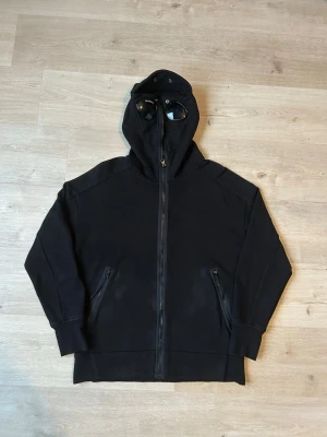 Svart CP Company Zip Hoodie - Fin Cp Company zip tröja med goggles i svart färg. | Tröjan är i mycket bra skick och sparsamt använd. |  Äkta som allt annat jag säljer!✅|  Storlek: M | Skick: Mycket Bra Skick  | Färg: Svart | Märke: CP Company | Modell: Sweatshirt, hoodie  |  Hör gärna av dig vid frågor så svarar jag så fort jag kan! 😁|