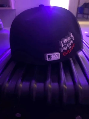 Svart New Era White Sox keps - Säljer en svart New Era 59FIFTY keps med White Sox-logga i vitt framtill. Baksidan har broderad text 'LOVE HUSTLE GAME' i vitt och rött. Klassisk flat brim och MLB-logga bak. Perfekt för dig som gillar streetwear och sportig stil.