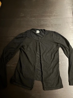 Svart kofta från Saint Tropez - Stilren svart kofta från Saint Tropez med rund halsringning och knäppning framtill. Tunn och mjuk kvalitet som passar perfekt till lager på lager. Långärmad modell som är enkel att matcha med olika outfits.