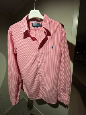 Ralph Lauren Skjorta - Säljer en riktigt stilren, trendig skjorta med röd vita ränder från Ralph Lauren. Perfekt till sommaren 2026! Storlek: L (Kom ihåg att den är slim fit). Skriv vid frågor, öppen med bud!