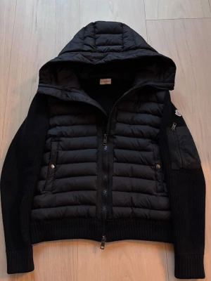 Moncler Cardigan  - En riktigt snygg svart Moncler Cardigan med en huva. Den är i storlek M men skulle säga att den passar som bäst på folk runt 180 och neråt! Kan gå ner lite i pris vid snabb affär! 