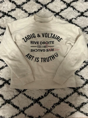 Vit sweatshirt Zadig & Voltaire🌟😍 - Vit sweatshirt från Zadig & Voltaire med svart tryck på bröstet där det står 'Art is Truth', 'Rive Droite' och 'Est. 1997'. Tröjan har rund halsringning, långa ärmar och en avslappnad passform. Det finns även ett litet dödskalletryck framtill. Tröjan har en liten defekt!!!!