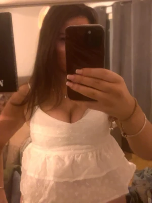 Fest toppVit volangig linnetopp - Söt vit linnetopp med volangdetaljer och v-ringning. Toppen är ärmlös och har tunna axelband, perfekt för varma dagar. Materialet känns lätt och luftigt, och toppen har en feminin och fräsch look.