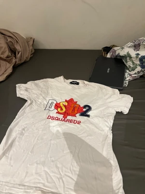 Vit DSQUARED2 t-shirt med tryck - Vit t-shirt från DSQUARED2 med stort färgglatt tryck på bröstet i rött, gult och blått. Klassisk passform och rund halsringning. Perfekt för dig som gillar streetwear och vill sticka ut med en ikonisk logga.