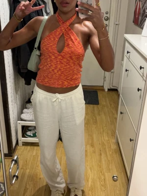 Orange topp - Säljer en orange och röd croppad halterneck topp med twistad front och nyckelhålsdetalj. Toppen är ärmlös och har ett coolt, melerat mönster. Perfekt för sommaren 🧡