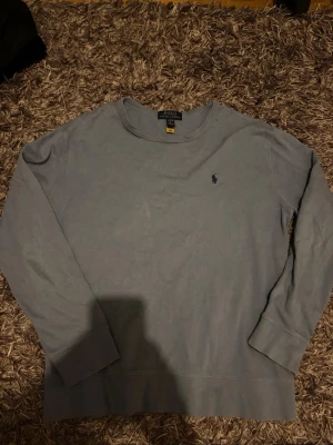 Ljusblå sweatshirt från Polo Ralph Lauren - En stilren ljusblå sweatshirt från Polo Ralph Lauren med rund halsringning och diskret broderad logga på bröstet. Tröjan har långa ärmar och en avslappnad passform, perfekt för en casual look.