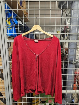 Röd kofta med paljettdetaljer och knyt - Röd kofta i viskosmix med långa ärmar och v-ringning. Dekorerad med små paljetter längs kanten och ett snyggt knyt framtill. Perfekt för dig som vill ha något extra till din outfit.