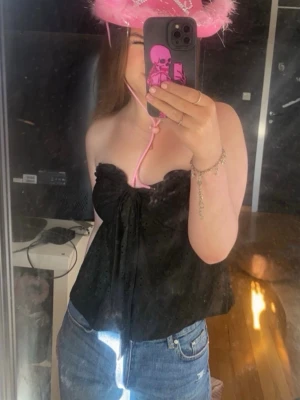 Svart axelbandslös tubtopp med knyt - Säljer en svart axelbandslös tubtopp med snygg knyt-detalj framtill. Toppen har en luftig passform och är perfekt till jeans eller kjol. Enkel men ändå trendig, passar dig som vill ha en stilren look.