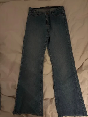 Blå raka jeans med rå kant - Säljer ett par blå jeans med rak passform och rå, fransig kant nedtill. Klassisk femficksmodell i jeansmaterial med normal midja. Perfekta för en avslappnad och trendig look.