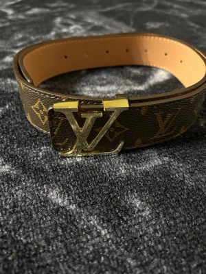 Brunt bälte med guldlogga - Snyggt brunt bälte med elegant guldlogga som ger en lyxig och trendig känsla. Detta är inte ett original, utan ett högkvalitativt alternativ med stilren design och fina detaljer. Perfekt för dig som vill lyfta din outfit och få en exklusiv look utan att betala premiumpris. Passar lika bra till jeans som till mer uppklädda outfits. Ett modernt och stilfullt bälte som verkligen gör skillnad.Pris ej hugget i sten . Längd 105 cm.