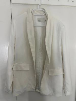 Kavaj - Stilren vit kavaj från NLY Trend med klassisk krage och två fickor framtill. Perfekt för att lyfta din outfit med en fräsch och modern touch. Använd men fortfarande i bra skick. Liten fläck på högra armen som ni kan se på andra bilden.